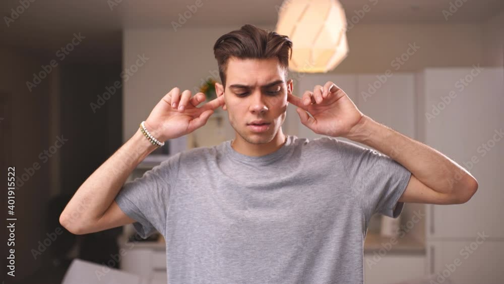 Portrait of a young man in casual clothing, covering his ears with his fingers from loud noises. Noisy neighbors Portrait of a young man in casual clothing, covering his ears with his fingers from loud noises. Noisy neighbors