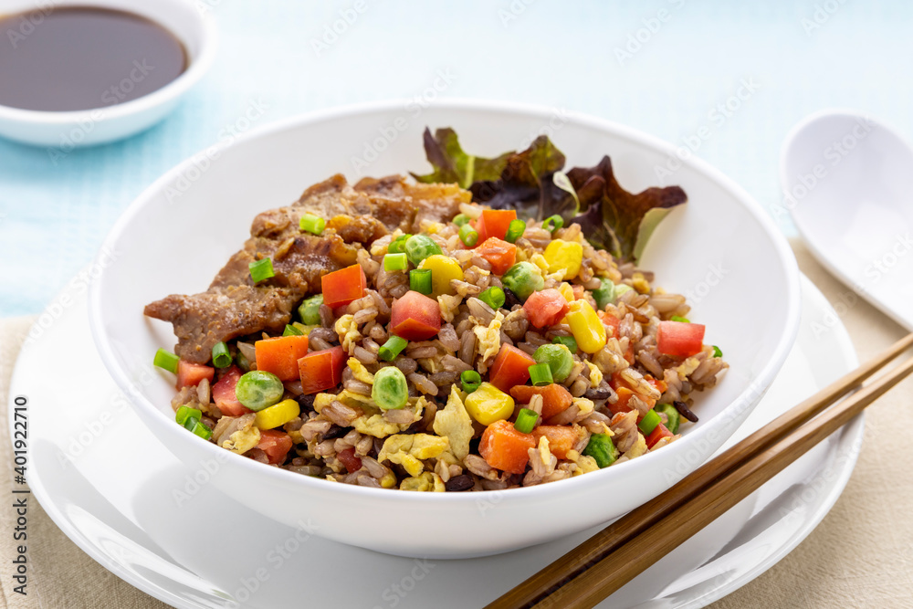 Fried brown rice with colorful vegetables, topped with fried pork Fried brown rice with colorful vegetables, topped with fried pork