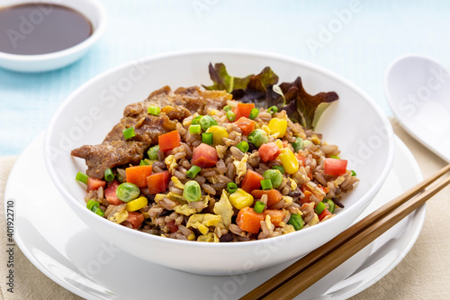 Fried brown rice with colorful vegetables, topped with fried pork