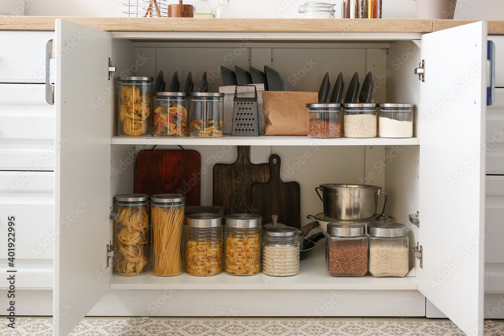 Shelves with utensils and glass jars with products in cupboard