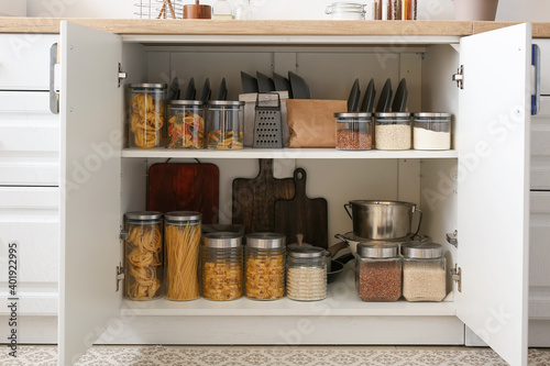 Shelves with utensils and glass jars with products in cupboard photo