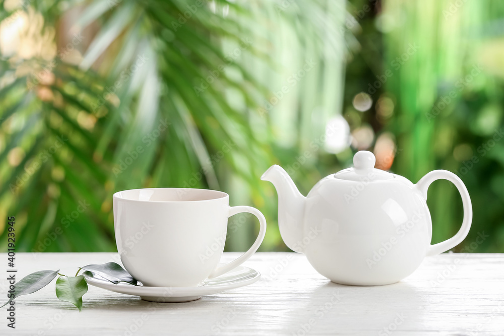 Cup of green tea and teapot on table against blurred background Cup of green tea and teapot on table against blurred background