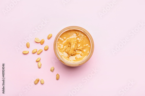 Jar with tasty peanut butter and nuts on color background