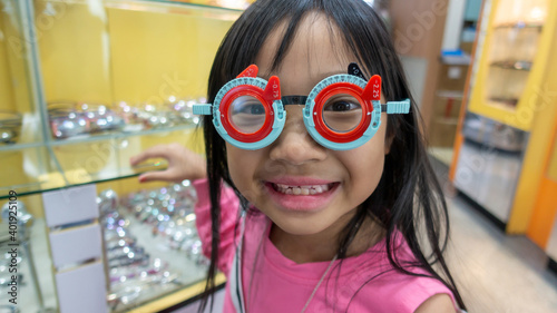 Asian child girl in an eyeglass shop wearing measuring glasses, pediatric refractive disorder