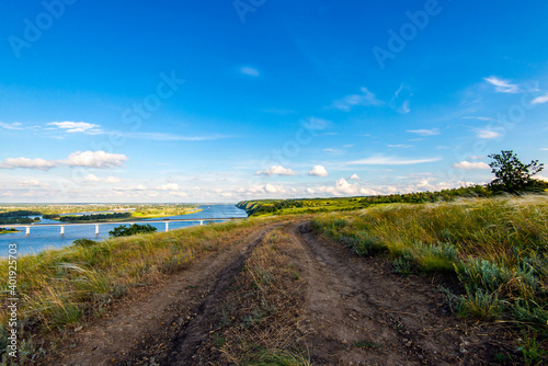 Dirt road in the steppe between feather fields grass and parallel with river