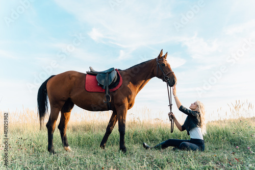 A girl in a field sits in front of a horse.