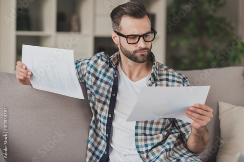 Photo of young handsome serious concentrated man look read analyze report paper documents sit sofa home remote work photo