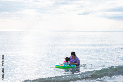 Father and daughter are playing in sea. Girl sitting on green raft. Father takes care of daughter. Little child held toy in his hand. During the summer or spring. Family activities build relationships © Kanthita