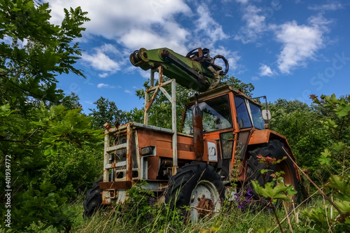 old rusty tractor in the green nature with clouds on the sky