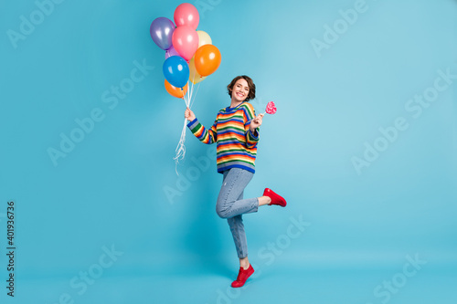 Full length body size view of cheery girl holding in hand air balls jumping eating heart candy isolated over pastel blue color background