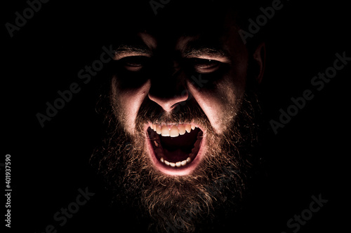 Angry  bearded man  shouting in rage from the darkness