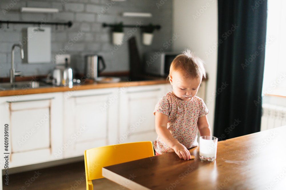 Caucasian cute toddler child with a glass of yogurt and cookies on a chair in a room in a real interior, funny grimy dirty children and healthy food, snack Caucasian cute toddler child with a glass of yogurt and cookies on a chair in a room in a real interior, funny grimy dirty children and healthy food, snack