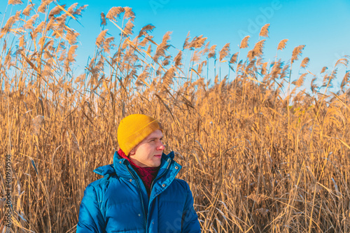 A man in a yellow winter hat stands against a background of fluffy reeds on a Sunny winter day. Beautiful natural background © KseniaJoyg