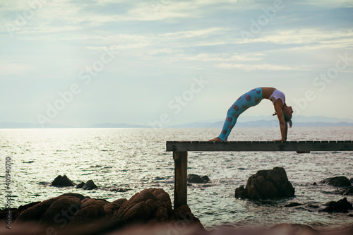 woman doing yoga pose on beach pier against cloudy sky