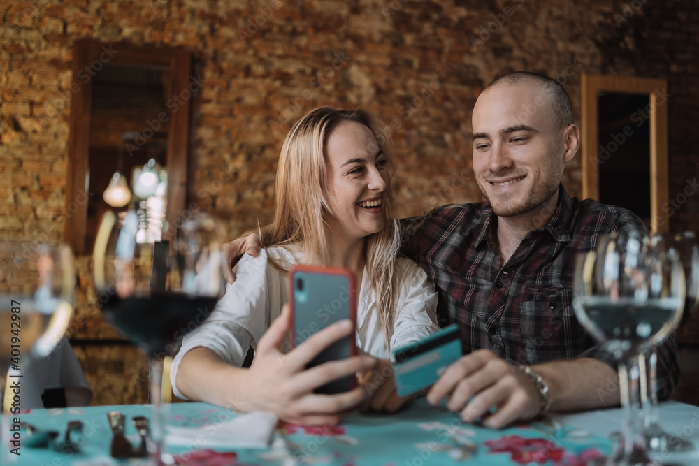 Fototapeta premium Happy couple enjoying dinner and paying the bill with a credit card - Young smiling couple shopping online together.