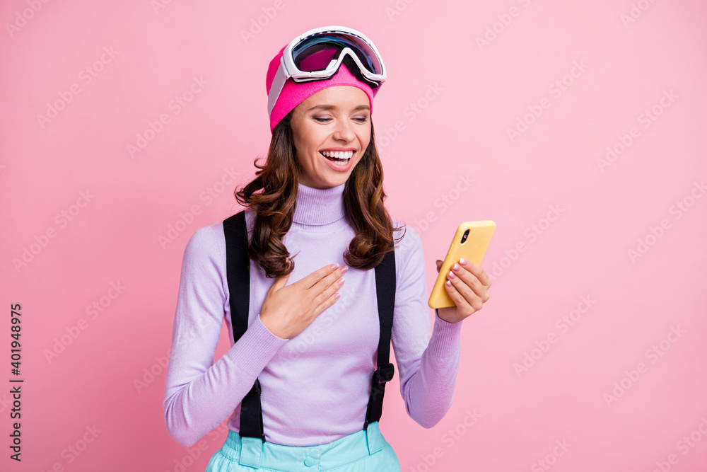 Photo portrait of laughing girl touching chest holding phone in one hand isolated on pastel pink colored background Photo portrait of laughing girl touching chest holding phone in one hand isolated on pastel pink colored background