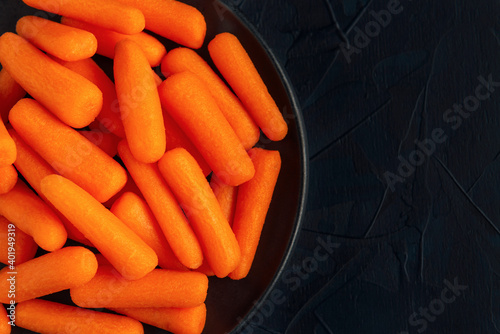 Black plate with small peeled pieces of carrot on dark textured backdrop. Top view. Space for text. photo