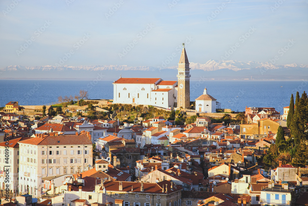 Fototapeta premium Red roofs of the historical center of old town Piran with main church against the sunset sky and Adriatic sea. Aerial view, Slovenia