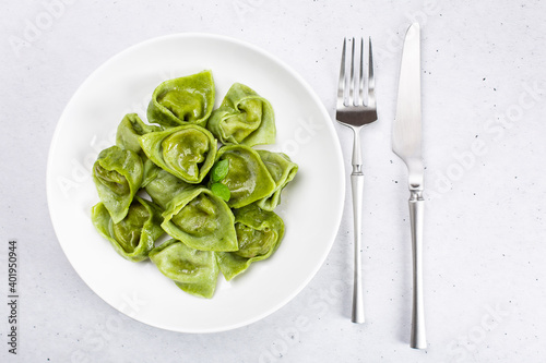 Homemade tortelli - italian green pasta  dough made with eggs and spinach   filled with ricotta and spinach. White plate and cutlery. Light background. Top view.
