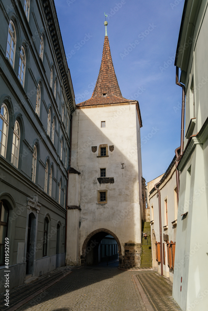 Gothic tower of the Velvary Gate, town fortifications built in the pre-Hussite period in sunny day, street of historic medieval city Slany, Central Bohemia, Czech Republic