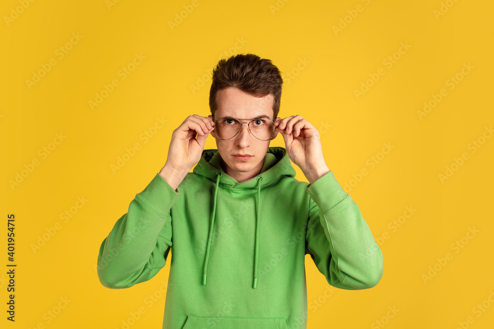 Eyewear. Caucasian young man's portrait on yellow studio background. Beautiful male model in green outfit gesturing. Concept of human emotions, facial expression, sales, ad, youth. Copyspace. Eyewear. Caucasian young man's portrait on yellow studio background. Beautiful male model in green outfit gesturing. Concept of human emotions, facial expression, sales, ad, youth. Copyspace.