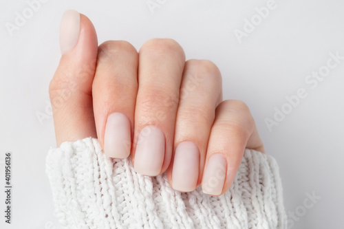 Matt nude nails close up on the light background. Winter manicure, woman hand in the warm sweater