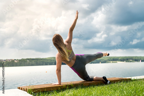 Young woman in sportwear doing fitness exercises outdoor near the lake