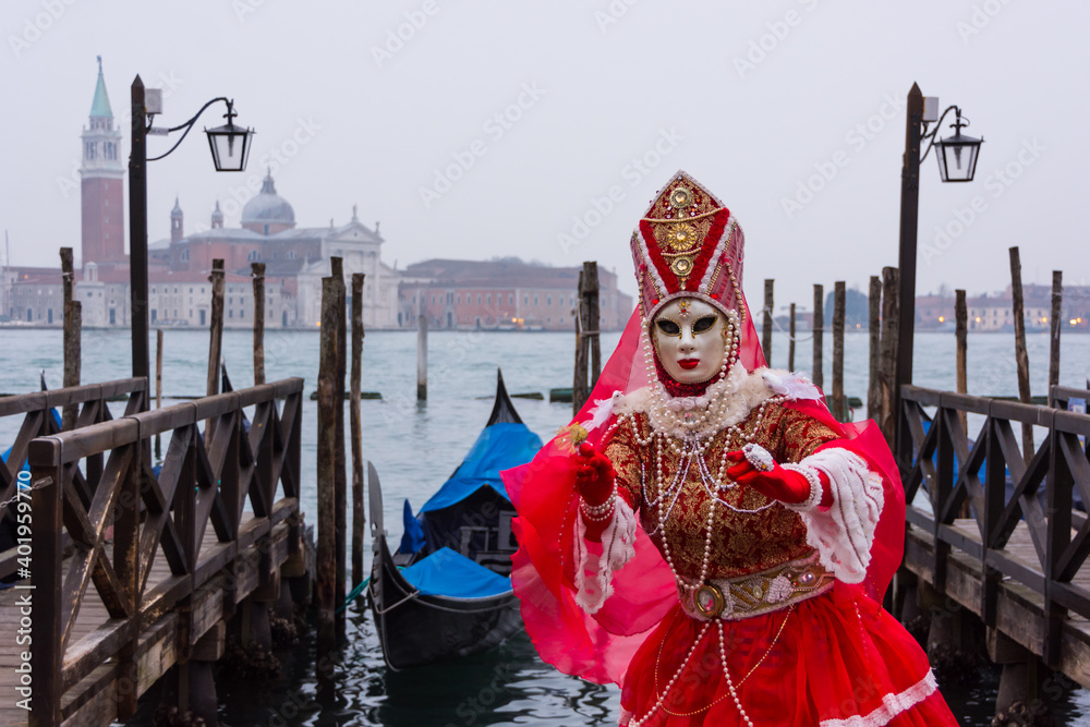 Venice, Italy - February 18, 2020: An unidentified woman in a carnival costume in front of a group of gondolas and St Giorgio's Island,  attends at the Carnival of Venice.