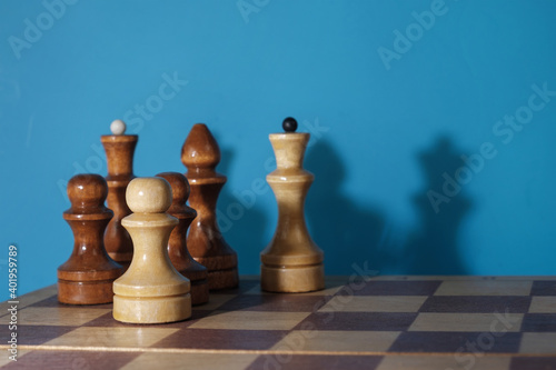 Wooden chess pieces and a chessboard with drop shadows on the blue wall, selective focus