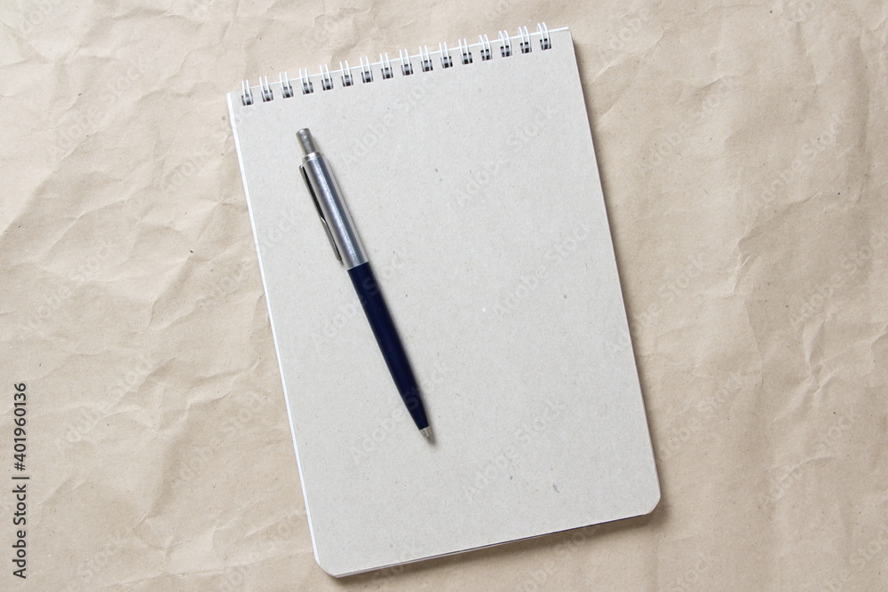 Gray notepad with white coiled spring and pen on a background of beige crumpled craft paper. With empty space for text and design Gray notepad with white coiled spring and pen on a background of beige crumpled craft paper. With empty space for text and design