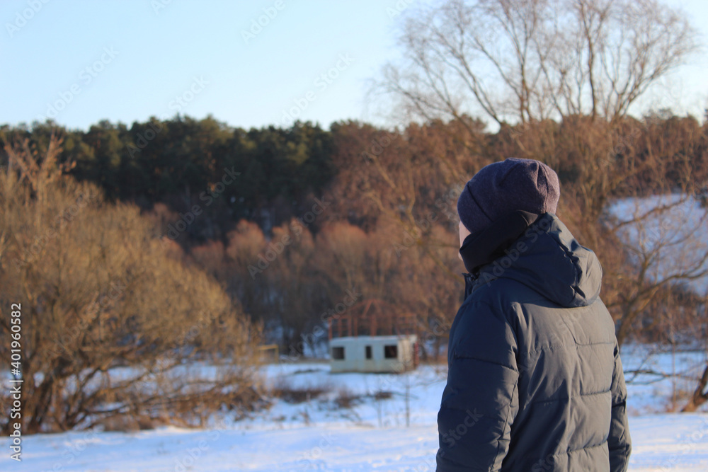 the man stands with his back to the camera and looks into the distance against the background of a snowy landscape