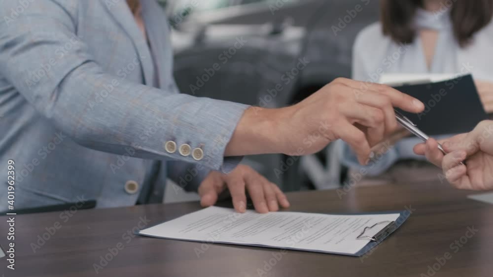 PAN close up of customers signing purchase agreement in dealership and buying new car