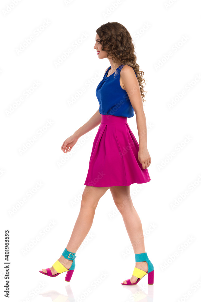 Walking Young Woman In Colorful High Heels, Pink Mini Skirt And Blue Top. Side View. Walking Young Woman In Colorful High Heels, Pink Mini Skirt And Blue Top. Side View.