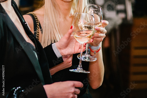 Glasses of wine in the hands of women. Clinking glasses with white wine and toasting.