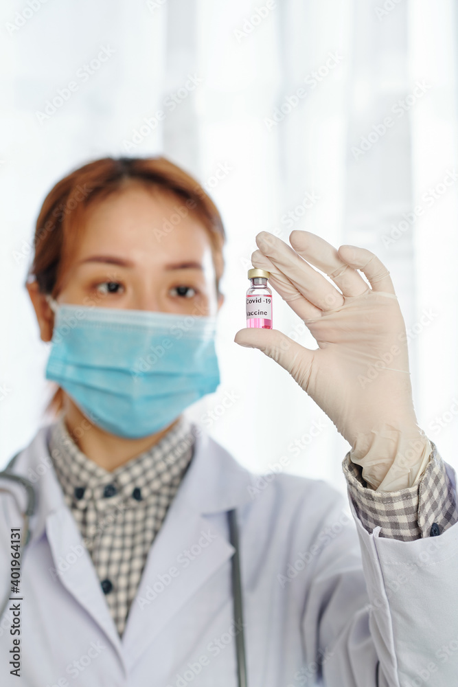 Young serious female physician looking at vial with vaccine against coronavirus in her hand