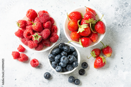 Fototapeta Naklejka Na Ścianę i Meble -  Ripe berries. Different berries in white ceramic bowls on a light table. Strawberries, raspberries and blueberries in plates