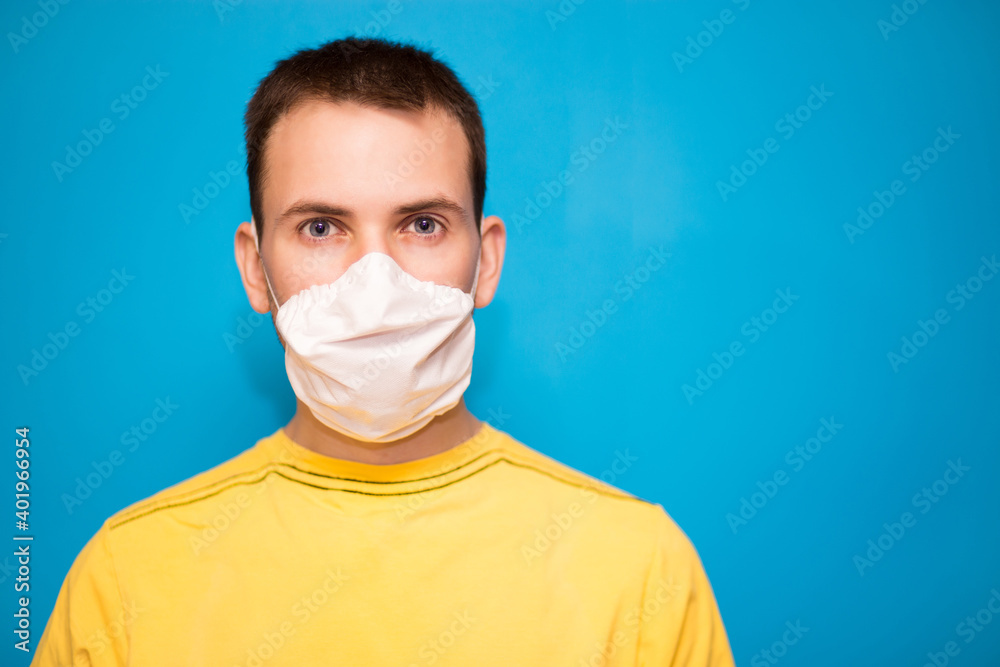 Portrait of tired young man in white medical mask on face for personal protection of coronavirus COVID-19 pandemic isolated on blue background. Exhausted confident person wearing protective face mask. Portrait of tired young man in white medical mask on face for personal protection of coronavirus COVID-19 pandemic isolated on blue background. Exhausted confident person wearing protective face mask.