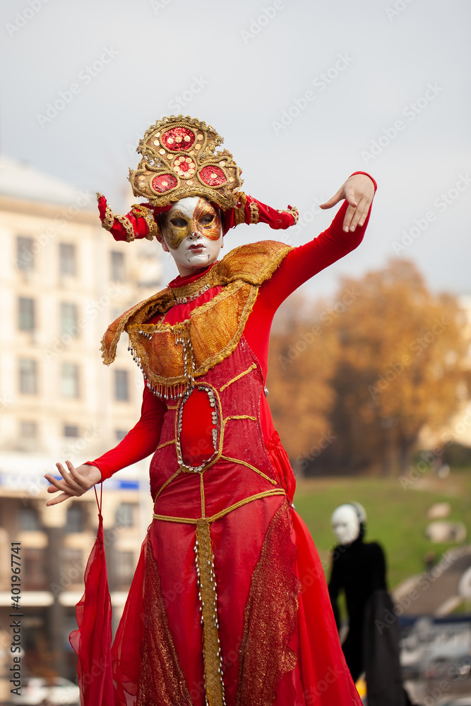 Man in a red carnival costume on stilts against the background of the cityscape