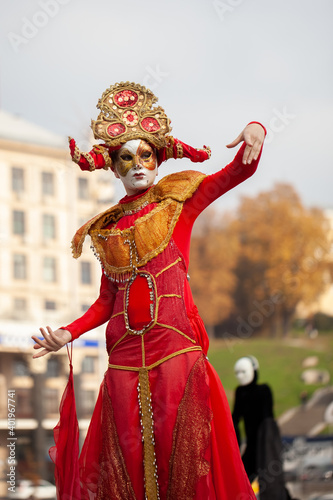 Man in a red carnival costume on stilts against the background of the cityscape