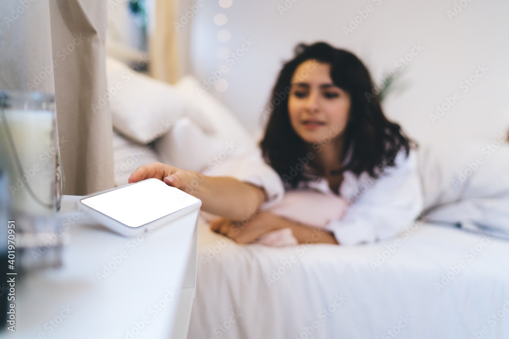Blurred female checking time on blank smartphone gadget with copy space area for text advertising using home internet connection in bedroom, woman turn off mobile alarm during lazy weekend day Blurred female checking time on blank smartphone gadget with copy space area for text advertising using home internet connection in bedroom, woman turn off mobile alarm during lazy weekend day