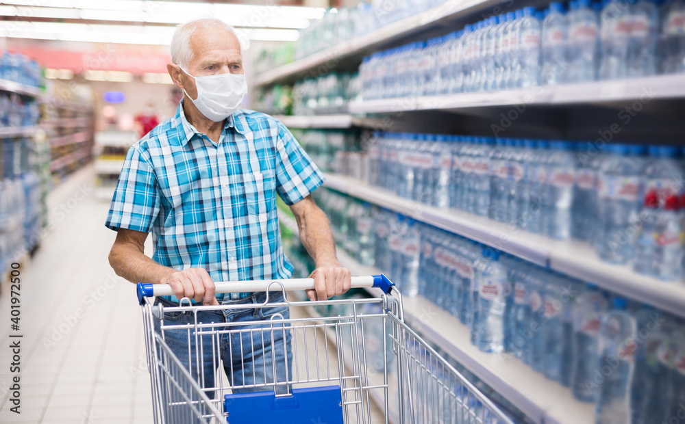 elderly european man in mask with covid protection selects bottled water in department of supermarket elderly european man in mask with covid protection selects bottled water in department of supermarket
