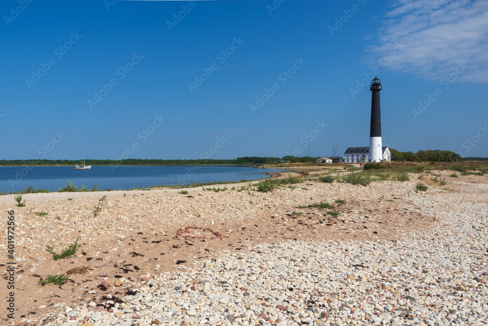 View to the Sõrve lighthouse in Saaremaa island, Estonia. Beach with sand and pebbles in the foreground. Focus on heart made from red pebbles on the sand in the foreground
