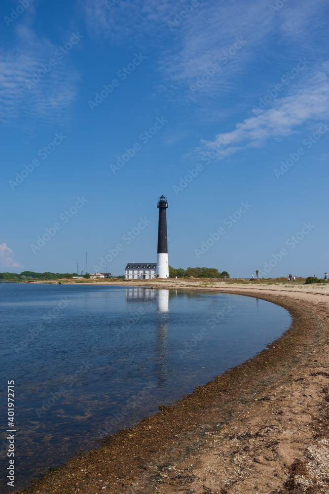 

View to the beach of Sõrve peninsula cape with sand and pebbles by coastline. Lighthouse in the background. Focus on water and pebbles in foreground