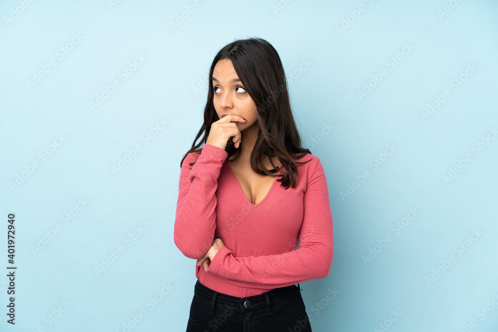Young mixed race woman isolated on blue background having doubts and with confuse face expression Young mixed race woman isolated on blue background having doubts and with confuse face expression