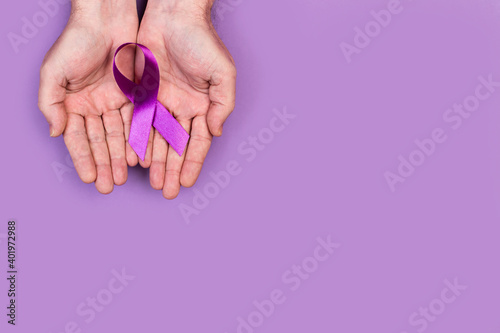 Manos de mujer sosteniendo una cinta lazo morado sobre fondo de color morado liso y aislado. Vista superior. Copy space. Concepto: Cancer photo