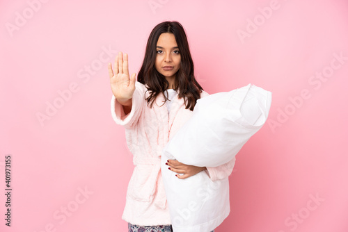 Young woman in pajamas isolated on pink background making stop gesture and disappointed