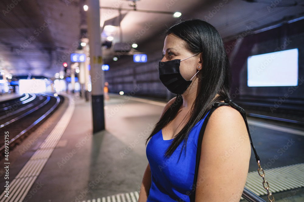 Young caucasian woman waiting the train in station while wearing protective face mask for coronavirus