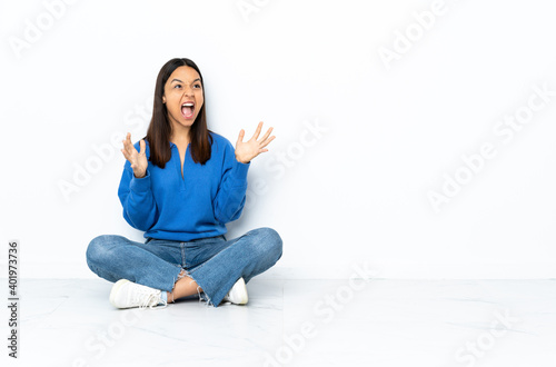 Young mixed race woman sitting on the floor isolated on white background with surprise facial expression