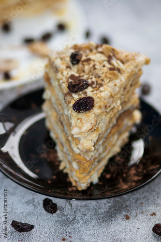 Napolion cake. A piece of cake on a black plate, decorated with raisins. Stands on a table with a gray background photo