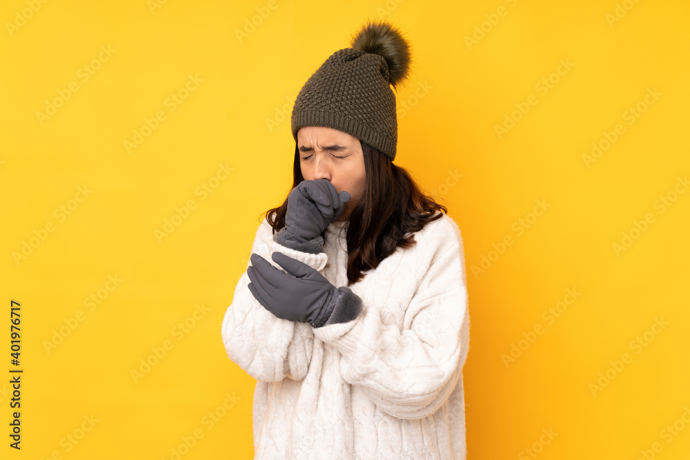 Obraz premium Young woman with winter hat over isolated yellow background is suffering with cough and feeling bad